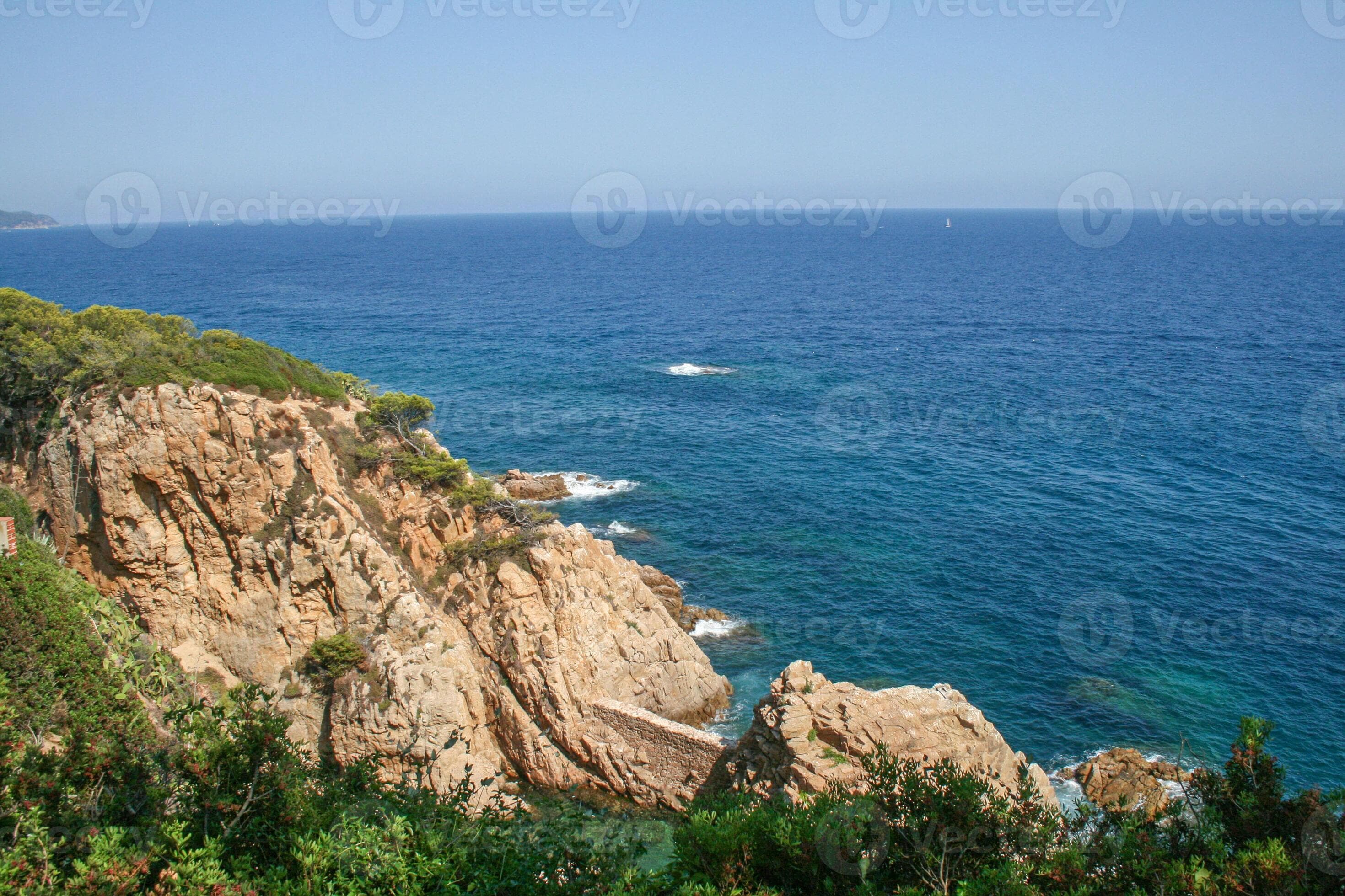 Scenic rocky shoreline with rugged cliff and green shrub overlooking deep blue sea under clear sky. Summer travel, nature and seaside landscape.