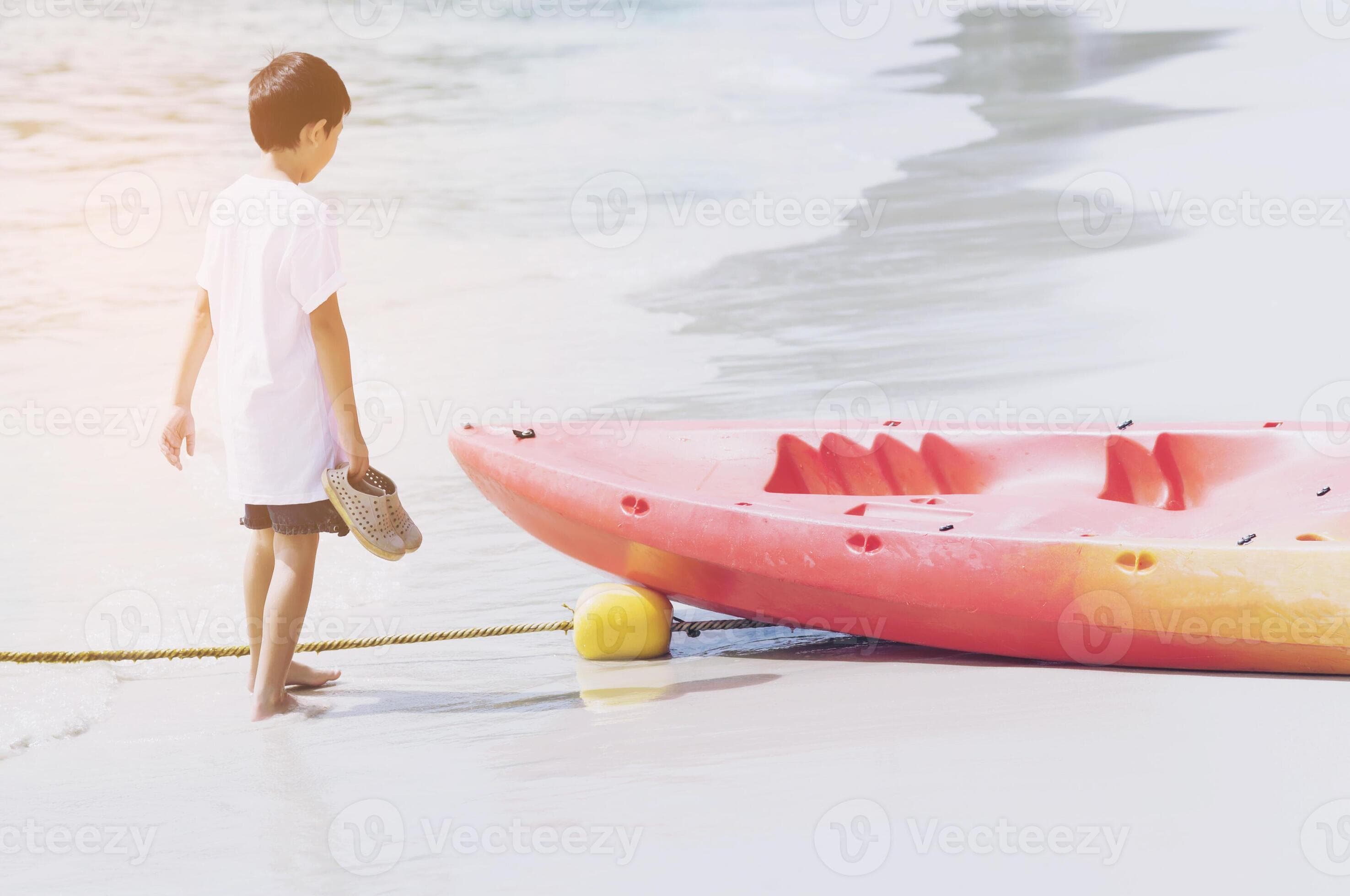 Kid walking and looking at canoe on beach