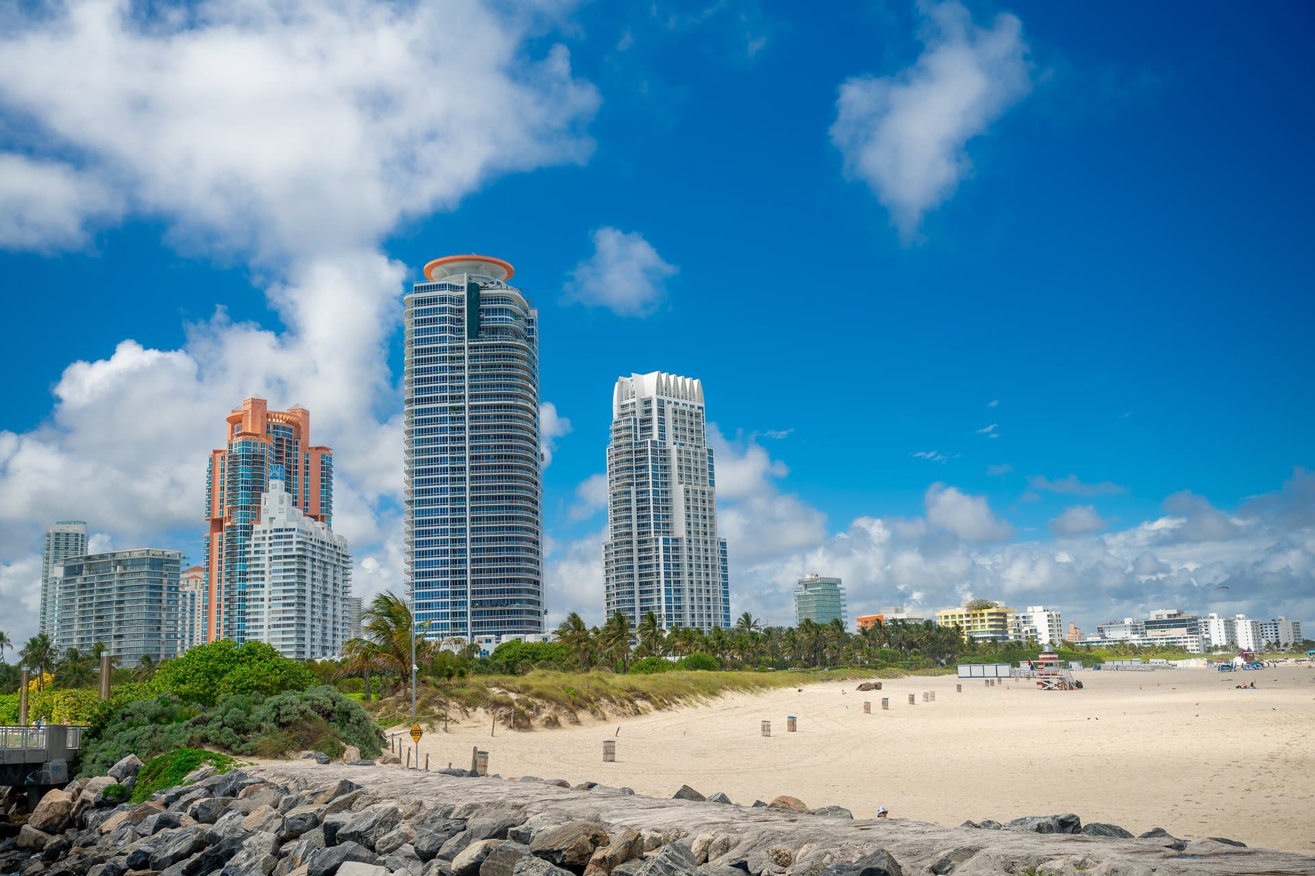 Modern high-rise apartment buildings and tropical park in Miami Beach. Perspective of tall residential towers behind a green field with palm trees under a cloudy sky in Miami.