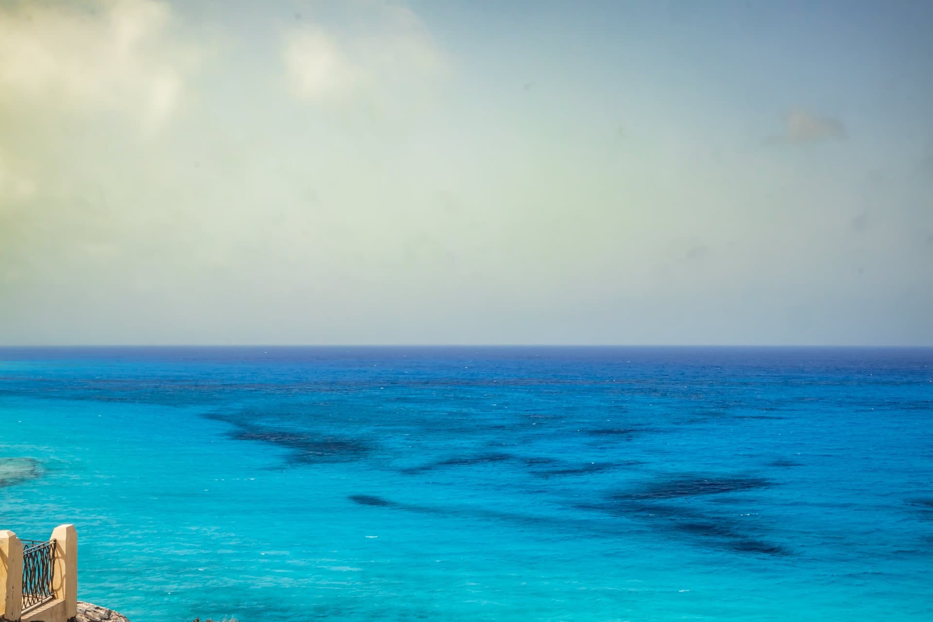 Tropical beach landscape with crystal clear turquoise ocean water, white sandy shoreline and dramatic cloud formations beneath a vivid blue sky in bright daylight