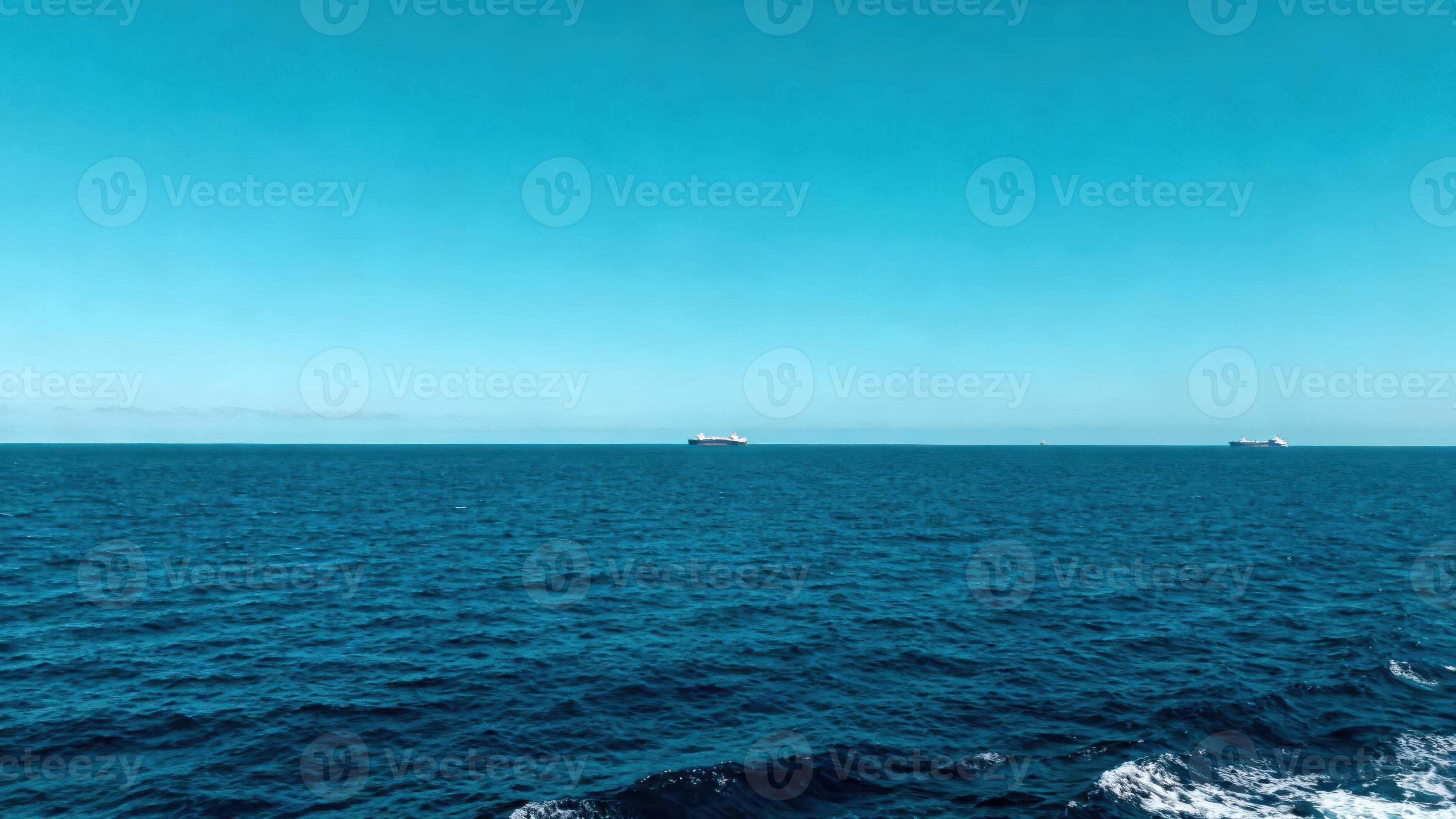 Vast deep blue ocean meets clear bright cyan sky with distant cargo vessels visible on the horizon